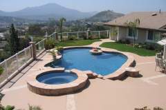 free-form-pool-with-raised-cascading-spa-poolside-fire-ring-quartzite-coping-water-sconces-colored-concrete-deck-with-quartzite-ribbons-and-dark-gray-interior-finish